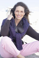 Long-haired woman in a dark coat with a sweater over her shoulders on the beach