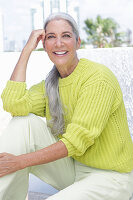 Grauhaarige Frau in grüngelbem Strickpullover und heller Hose