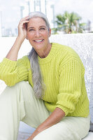 Gray-haired woman in a green-yellow knit sweater and light-colored trousers