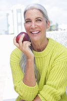 Grauhaarige Frau mit einem Apfel in grüngelbem Strickpullover