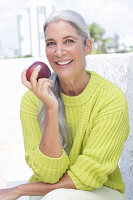 Gray-haired woman with an apple in a green and yellow knit sweater