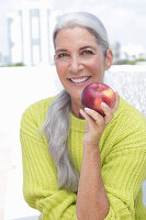 Grauhaarige Frau mit einem Apfel in grüngelbem Strickpullover