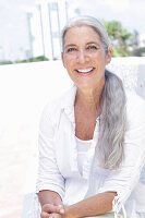A woman with long grey hair wearing a white blouse