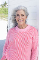 Grauhaarige Frau in pinkfarbenem Pullover am Strand