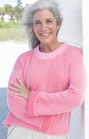 Grauhaarige Frau in pinkfarbenem Pullover am Strand