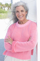 Grauhaarige Frau in pinkfarbenem Pullover am Strand