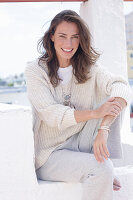 Happy, long-haired woman in light, casual knitted jumper and trousers