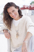 A happy, long-haired woman wearing a light-coloured, casual knitted jumper