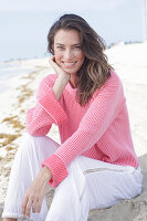 A long-haired woman wearing a pink jumper and white trousers