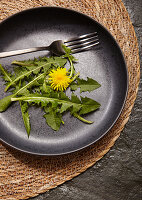 Dandelion salad with a blossom on a black plate