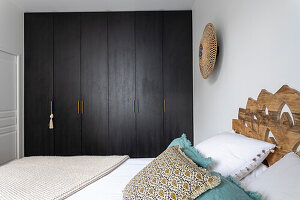 Double bed with headboard of decoratively carved wooden panels and wardrobe with dark fronts