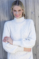 Young blond woman in white knitted jumper in front of board wall