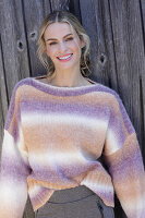 Young blond woman in knitted jumper with colour gradient in front of board wall