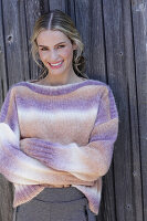 Young blond woman in knitted jumper with colour gradient in front of board wall