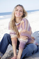 Junge blonde Frau im Strickpullover mit Farbverlauf und Jeans am Meer