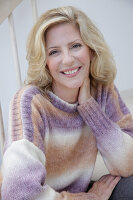 A mature blonde woman wearing a knitted colour gradient jumper