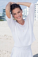 Fröhliche Frau im weißen Pullover und weißer Hose am Strand