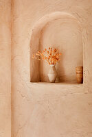 Vase with dried flowers in round-arched wall niche with peach-colored plaster work