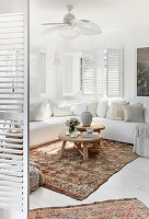 Weiße Sitzmöbel mit Leinenbezug, Fensterläden und marokkanische Teppiche im Wohnzimmer