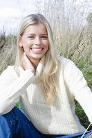 Junge blonde Frau in weißem Rollkragenpullover und Jeans in der Natur