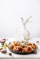 Homemade Easter traditional hot cross buns in ceramic dish with blossom flowers, chocolate candy and quail eggs