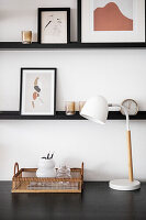 Black shelves with pictures on white wall above a desk