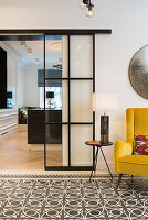 Yellow retro armchair with side table on cement tiles, sliding glass door to the kitchen