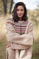 A brunette woman outside wearing a knitted jumper and a dusty pink coat