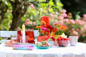 Table with colorful vases, flowers, drinks, and candles in the garden