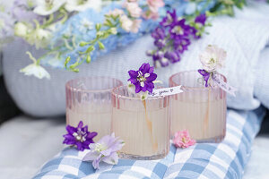 Drei Gläser Limonade dekoriert mit Blumen und Schildchen auf kariertem Stoff