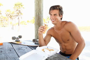 A young topless man eating a sandwich