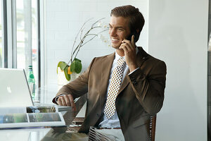 A young businessman wearing a brown blazer on the phone in an office