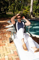 Young man with a beard in a polo shirt and white pants is sitting on a lounger