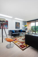 Black leather couch, tripod lamp, and vintage chair in bright living room with terrace access