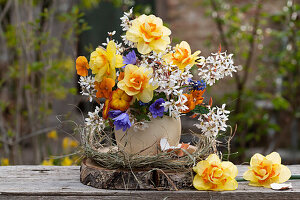 Blumenvase mit Kronen-Anemone (Anemone coronaria), Narzissen (Narcissus), Primeln, Felsenbirnen (Amelanchier) auf Holzscheibe