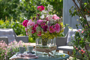 Bouquet of roses with goutweed and lady's mantle in glass vase on patio table