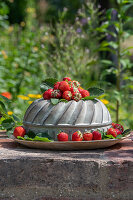 Cake tin decorated with fresh strawberries on wall in garden
