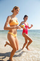 Girl friends playing volleyball while jogging at the sea