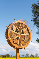 Insect hotel in the shape of a steering wheel at the edge of a rape field