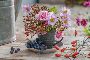Autumn bouquet with rose hips, pink roses and autumn anemones in cup