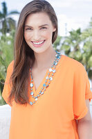 A cheerful young woman wearing an orange summer blouse with a necklace