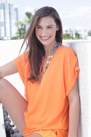 A cheerful young woman wearing an orange summer blouse with a necklace