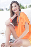 A cheerful young woman wearing an orange summer blouse with a necklace