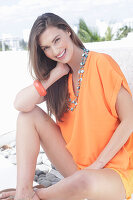 A cheerful young woman wearing an orange summer blouse with a necklace