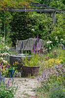 Water fountain in the summer garden, behind it garden place with pergola and wooden bench