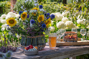 Sommerlicher Blumenstrauß mit Sonnenblumen, Kugeldisteln, großer Bibernelle, Bienenfreund, Oregano und Kosmeen auf Holztisch im Garten