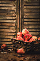 Rote Äpfel in Korb vor Holzwand