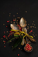 Coriander, mustard seeds and pink pepper on three silver spoons with bay leaves