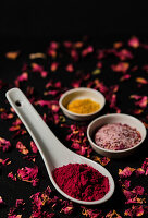 Beetroot powder on white porcelain spoon next to a small bowl with flower salt with rose petals