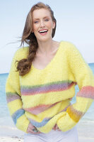 Young, blond woman in yellow jumper with coloured stripes and white trousers at the seaside